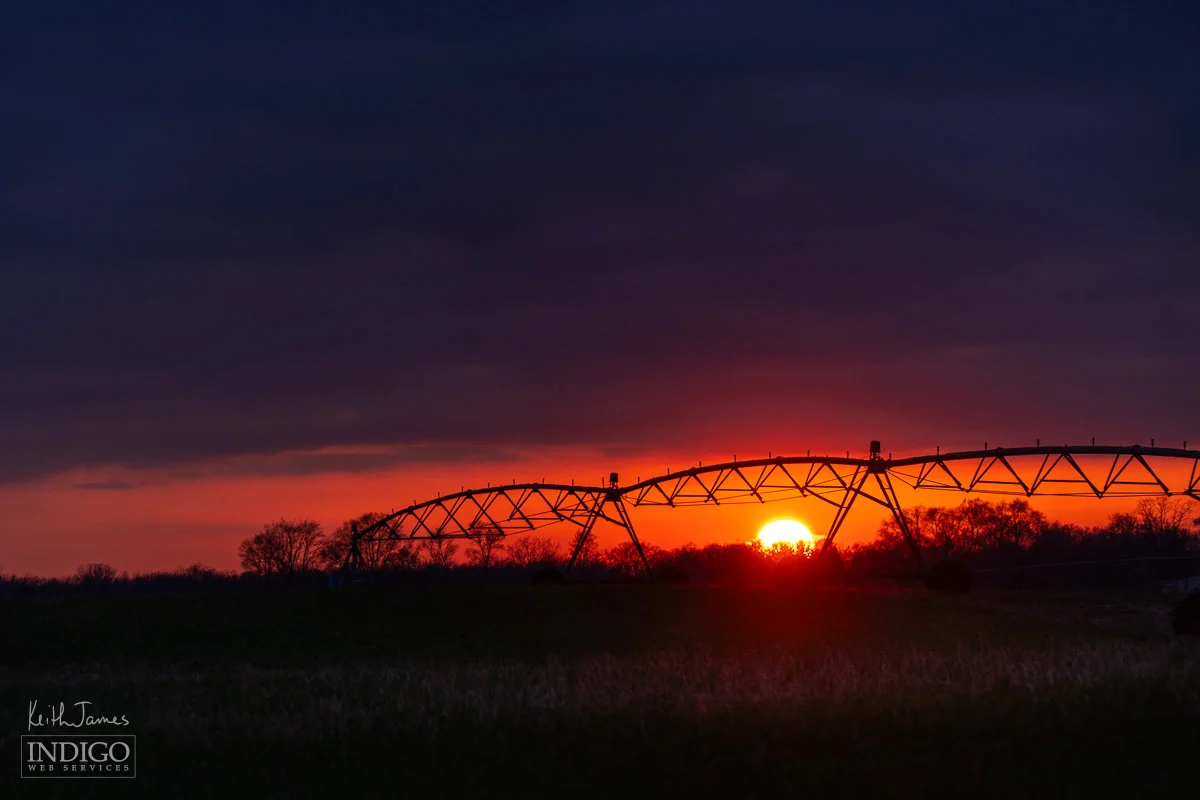 Silhouette of an irrigation pivot against a sunset sky.