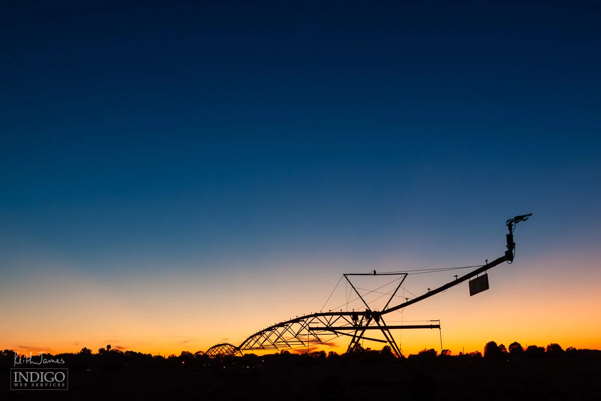 Silhouette of an irrigation pivot against a sunset sky.