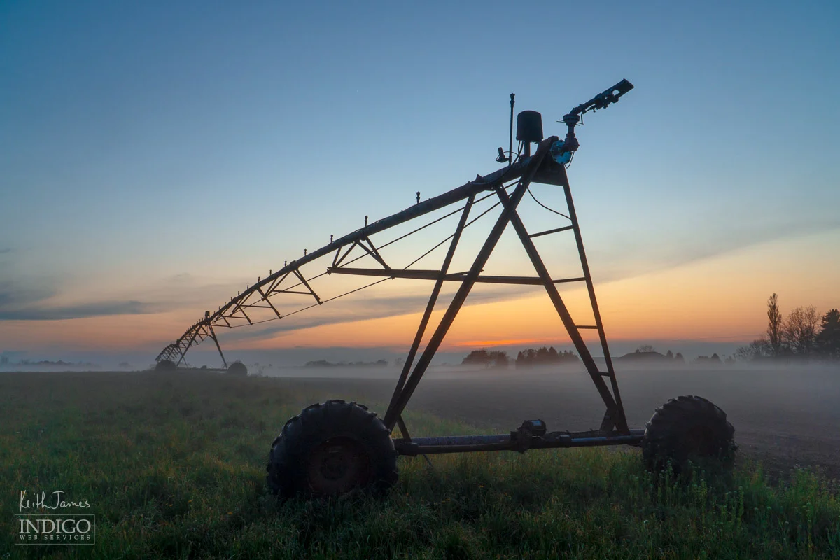 An irrigation pivot with low fog along the ground at sunset.