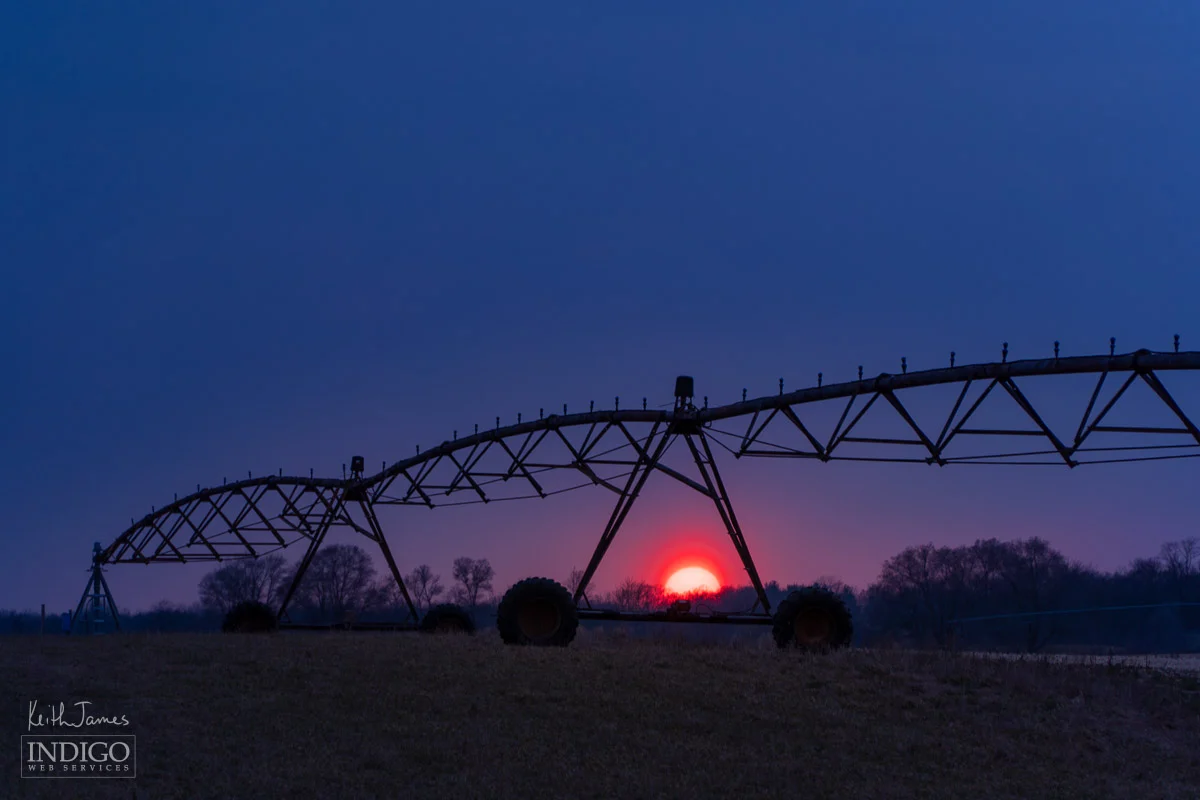 Silhouette of an irrigation pivot against a sunset sky.
